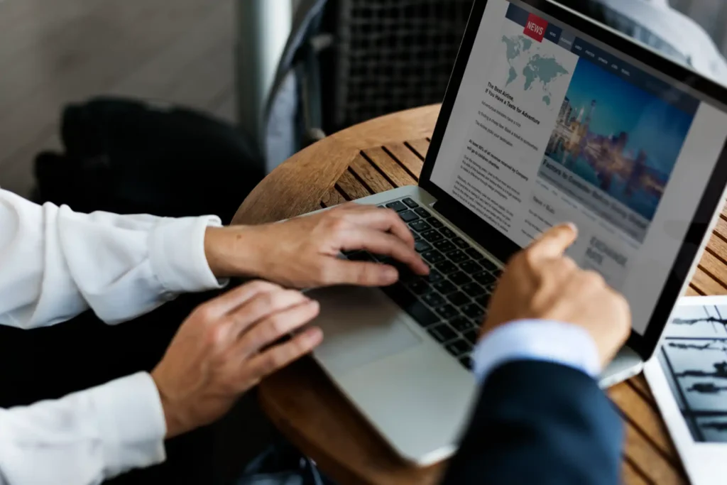 Imagem de duas pessoas utilizando um laptop para acessar informações sobre Google Discover e Google News em um ambiente de trabalho.