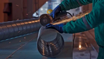 Imagem de um profissional realizando corte em tubo de metal com equipamento de solda, envolvendo trabalho de tratamento térmico de metais.